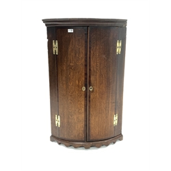 18th century George III oak bow front wall hanging corner cupboard, projecting cornice over two mahogany cross banded doors enclosing three shelves,