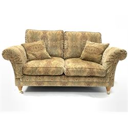 Parker Knoll - two seat sofa, upholstered in golden medallion fabric, with two small cushions and supported by two brass castors. W 180cm, height to seat 49cm. 
