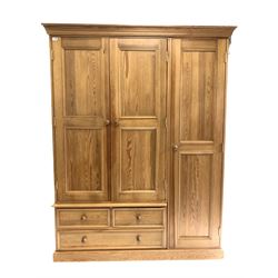Polished pine triple wardrobe, full length panel door enclosing interior fitted for hanging, flanked by two further cupboard doors, over two short and one long drawer 