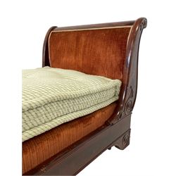 French Empire period figured mahogany lit bateau or sleigh day bed, the shaped rolled uprights decorated with applied scrolling decoration, figured frieze rail on bracket feet decorated with scrolling and carved stylised foliage, upholstered in burnt orange fabric with base and squab cushion 