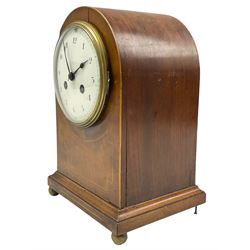 An Edwardian mantle clock in an arched mahogany case inlaid with satinwood stringing on a moulded plinth with ball feet (one missing), arched rear door with brass sound fret, eight-day French striking movement with a recoil anchor escapement striking the hours and half hours on a coiled gong, with a white convex enamel dial, upright Arabic numerals and minute track, steel spade hands within a cast bezel and convex glass. With pendulum.
H 26 W 19 D14