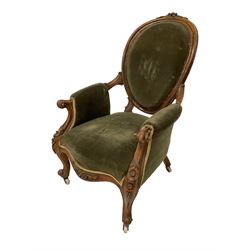 Victorian walnut open armchair, the cresting rail carved with flower heads and extending foliage, oval back with moulded frame, upholstered in green fabric, scrolled arm terminals on shaped supports carved with flower heads, cabriole front feet, on brass and ceramic castors