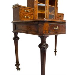 19th century figured walnut lady's writing desk or Bonheur du Jour, raised cabinet enclosed by two glazed doors flanked by smaller drawer, decorated with cast gilt metal mounts and gallery, moulded rectangular top with inset leather over two drawers, turned and fluted supports carved with trailing foliage and terminating to lobe feet, on brass castors