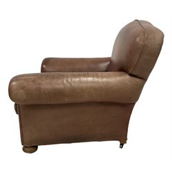 Pair of early 20th century club armchairs, traditional shape with rolled arms, upholstered in tan leather with loose seat cushion, on compressed bun feet with castors