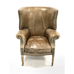 Georgian design barrel back wing armchair, upholstered in studded tan leather, with squab cushion, raised on square tapered supports terminating in brass castors, 