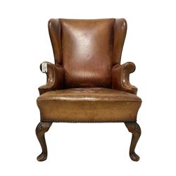 Georgian design wingback armchair, high back over down-scrolled arms, upholstered in tan leather with studwork border, raised on cabriole supports with shell moulded knees