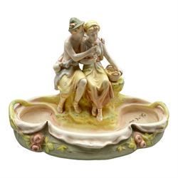 Royal Dux figural posy bowl surmounted by a seated courting couple with a basket of flowers on a quatrefoil shaped twin handled dish, post 1918 marks beneath, W39cm x H30cm 
