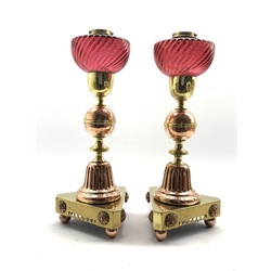  Pair of Victorian Arts and Crafts style brass and copper oil Lamps with cranberry glass reservoirs and on triangular bases with pierced and floral decoration, H55cm  