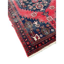 Persian Hamadan crimson ground rug, the field decorated with geometric and stylised plant motifs, the main border decorated with flower heads within geometric guard stripes 