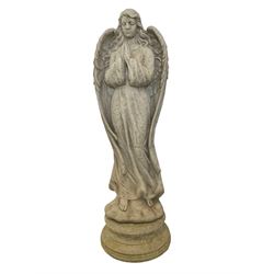 Composite stone garden figure modelled as a winged praying angel, raised on a circular plinth