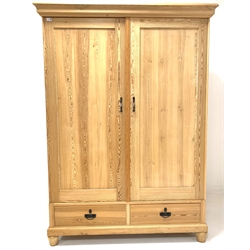 20th century stripped pine double wardrobe, projecting cornice over two panelled doors enclosing interior fitted for hanging, two drawers to base, raised on turned lobe carved front supports 