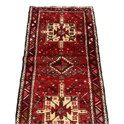 Persian Heriz red ground runner rug, the field decorated with large alternating geometric medallions surrounded by stylised tree of life and plant motifs, the guarded border with interlocking triangles of contrasting colour