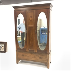 Edwardian inlaid mahogany double wardrobe, two oval mirrored doors enclosing interior fitted for hanging, one drawer under, raised on bracket supports, W125cm, H205cm, D50cm