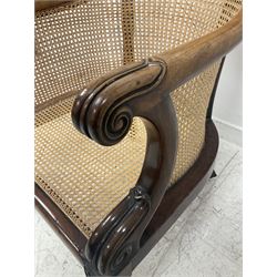 Victorian mahogany framed bergere armchair, the scrolled cresting rail and arms surrounding cane back and seat, raised on turned and reeded supports, terminating in brass castors  