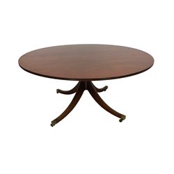 Georgian design mahogany dining table, the circular top with reeded edge, the pedestal carved with stepped turns terminating in a quadrupod base, the splayed sabre supports culminating in brass cups and castors