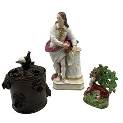 Early 19th century Derby porcelain figure modelled as John Milton, circa 1830,  leaning upon three books on a circular plinth, no. 297, 26cm, 19th century Staffordshire model of a recumbent stag and bocage, together with a 19th century Wetheriggs slipware tobacco jar with bird knop handle and tree stump decoration throughout, H17cm (3)
