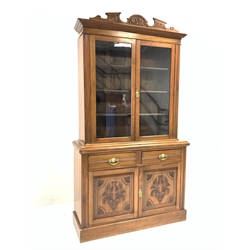  Edwardian walnut bookcase on cupboard, floral carved cornice over glazed doors enclosing three adjustable shelves, two drawers and cupboard under, plinth base, W121cm  