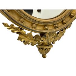 Regency design giltwood and gesso wall mirror, the carved eagle pediment holding a gilt sphere and chain in its beak, perched atop a rocky plateau on an acanthus leaf capital with a twin scrolling base with rosettes and extending oak leaves, the circular convex plate within a moulded frame with applied spherical mounts, the carved apron decorated with extending foliage and petal drop