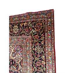 Persian Kashan red ground carpet, floral design shaped central medallion with scrolled borders, the field decorated profusely with scrolling foliage branches and stylised plant motifs, the repeating floral pattern border within guard bands