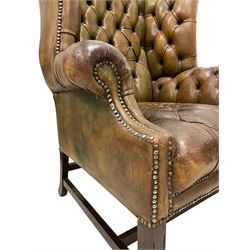 20th century Georgian design wingback club armchair, hardwood-framed and upholstered in deeply buttoned brown leather with stud work, on square supports united by H-stretchers 