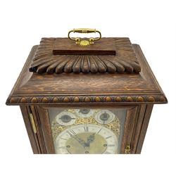 English – Edwardian oak 8-day bracket clock, three train fusee movement sounding the quarters on 8-bells and the hour on a coiled gong, flat top with egg and dart carving and carrying handle, fretted side panels and a fully glazed case door, conforming stepped plinth raised on brass feet, brass dial with foliate spandrels, serpentine hands and a silvered chapter ring, subsidiary dials for chime selection, pendulum regulation and chime/silent. With pendulum and key. 