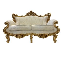 Silik Lo Stile Di Classe - Italian Rococo style carved gilt two seat wingback sofa, pierced pediment with scrolling cartouche and floral motifs with swept scroll uprights, upholstered in cream and gold foliate patterned fabric, raised on swept scrolled and flower head cabriole supports with cartouche aprons 