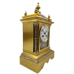 Early 20th century French mantle clock in a brass satin finished case with contrasting silvered detail, canted ogee top surmounted by a central pineapple finial, white enamel dial with Arabic numerals and steel trefoil hands above a porcelain panel depicting cupid and psyche, with flanking silvered Corinthian columns raised on a decoratively shaped rectangular plinth, eight-day countwheel striking movement, striking the hours and half hours on a gong.  With pendulum and key.
