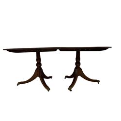 Regency design mahogany twin pedestal dining table, oval top with crossbanding and boxwood stringing, with reeded edge, raised on turned pedestals with tripod base, the splayed supports terminating in brass hairy paw feet and castors, with additional leaf