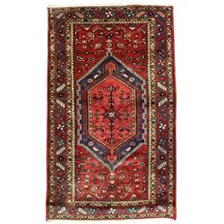 Persian Hamadan crimson ground rug, the field with a central indigo elongated lozenge containing secondary geometric patterns, surrounded by stylised plant and bird motifs, the multi-guarded border with repeating geometric designs and flowerheads