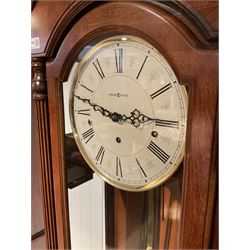 A 20th century American floor standing “tall case clock” with a swan’s neck pediment and full-length glazed trunk door flanked by reeded pilasters with capitals, cream dial inscribed “Howard Miller” with Roman numerals and serpentine hands within a gilt spun brass bezel, three train weight driven German movement chiming the quarters and striking the hours on eight gong rods, with strike/silent facility. With key, three brass cased weights and Gridiron pendulum.

