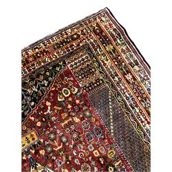 Persian red ground rug, the busy field decorated with a central floral pole medallion, surrounded by densely woven flower heads and floral designs, flanked by columns filled with lozenge patterns and foliate capitals, the heavily guarded multi-band border with repeating and contrasting geometric and floral motifs
