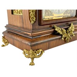 Reinhold Schneckenburger – German late 19th century 8-day mantle clock in a rosewood case, break arch pediment surmounted by an ogee carved top with gilt brass finials, conforming door with bevelled glass flanked by gilt caryatid to the corners, silk backed brass sound frets to the sides, with an ogee plinth raised on paw feet, brass dial with cast spandrels, matted dial centre and silvered chapter ring with Roman numerals, pendulum adjustment dial to the break arch and steel fleur di Lis hands, twin train going barrel movement striking the hours and quarters on two coiled gongs, makers trademark and serial number on movement backplate.
With pendulum and key.
