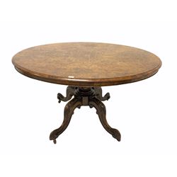 Victorian walnut breakfast table, the well figured oval tilt top raised on baluster turned column and four splayed, scrolled and leaf carved supports terminating in ceramic castors W137cm