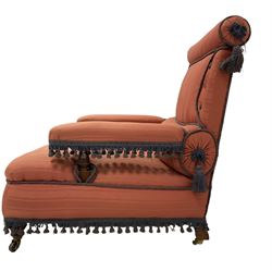 Late 19th century Howard design armchair, upholstered in coral pink striped fabric with indigo fringing, the cresting rail and lumber support with bolster design, raised on turned supports with castors