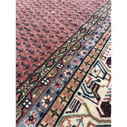Large Persian ground carpet, repeating motif on faded red field, enclosed by geometric design to multi line border 407cm x 302cm