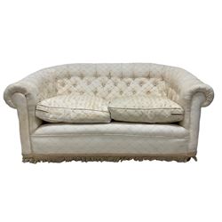 Pair chesterfield design two seat sofas, upholstered in buttoned cream fabric with butterfly pattern, fringe to base, on casters 