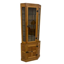 Mouseman - oak floor-standing corner cabinet, arcade carved cresting over lead glazed single door and uprights, the lower cupboard enclosed by panelled door with wrought metal fixtures, carved with mouse signature, on skirted base, by the workshop of Robert Thompson, Kilburn