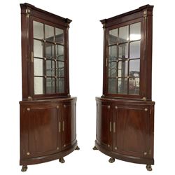 Pair of French Empire design corner cabinets, the straight-front upper section with canted corners and applied half-column pilasters, enclosed by mirror glazed door, the bow-front lower section enclosed by two doors with applied mouldings, mounted by cast metal floral rosettes, skirted base with cast gilt metal hairy paw brass feet