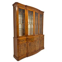 Yew wood shaped break-front display cabinet, the top section with projecting cornice over figured frieze, enclosed by four astragal glazed doors, with glass shelves, the lower section fitted with three drawers, double cupboard and two single cupboards, on plinth base