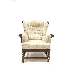 Ercol 'cloister' stained elm wingback armchair, with spindle back, fitted upholstered squab cushions, raised on turned and block supports united by stretchers W85cm