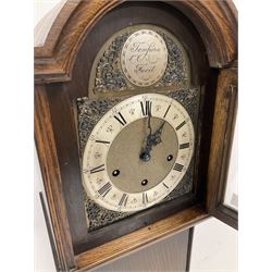 Plain dark oak cased “Grandmother” clock with a break arch top and conforming glazed hood door, with a stylised 18th century brass dial, spandrels, matted dial centre, silvered chapter ring and steel hands, case with a long trunk on a short square plinth, with an eight-day three train spring driven Westminster chiming movement. With pendulum.  