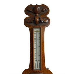 An oak cased aneroid barometer with carved relief c1930, with an 8” porcelain dial measuring atmospheric air pressure from 26 to 31.9 inches, weather predictions in Gothic and Roman script, with a brass indicating hand and steel recording hand within a brass bezel and flat glass, with a glazed thermometer box and mercury thermometer recording the temperature in degrees Celsius and Fahrenheit. 



