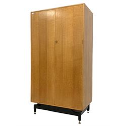 E Gomme for G-Plan - 'Brandon' range mid century vintage light oak double wardrobe, the two doors enclosing interior fitted with four shelves, two drawers and hanging rail, raised on turned ebonised supports W92cm, H172cm, D54cm