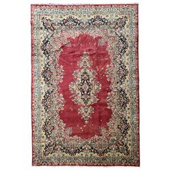 Persian Kerman red ground rug, the plain field with shaped floral medallion enclosed by a series of floral scrolls, the extending borders decorated with scrolling foliage branches and flowerheads