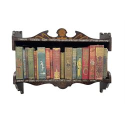 Early 20th century hanging bookshelf, the shelves decorated with brass wire motto and poker work decoration, with an assortment of cloth bound books, L59cm x H44cm