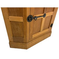 Mouseman - oak floor-standing corner cabinet, arcade carved cresting over lead glazed single door and uprights, the lower cupboard enclosed by panelled door with wrought metal fixtures, carved with mouse signature, on skirted base, by the workshop of Robert Thompson, Kilburn