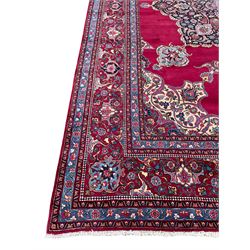 Large Persian Meshed red ground carpet, the plain field with large shaped central panel decorated with floral motifs, projecting stylised flower head medallions, the border decorated with repeating and scrolling stylised plant motifs