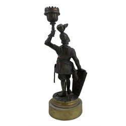 19th century French bronze candlestick modelled as a Knight, modelled as a standing wearing a plumed helmet and body armor, a shield in one hand and holding aloft a single sconce, on polished circular brass base, H27cm 