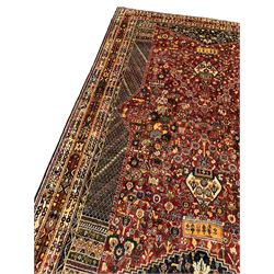 Persian red ground rug, the busy field decorated with a central floral pole medallion, surrounded by densely woven flower heads and floral designs, flanked by columns filled with lozenge patterns and foliate capitals, the heavily guarded multi-band border with repeating and contrasting geometric and floral motifs