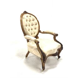 Late Victorian mahogany open armchair, floral carved crest rail over oval buttoned back, scrolled and leaf carved arm terminals, shaped apron and cabriole supports terminating in ceramic castors, upholstered in ivory floral damask, W64cm